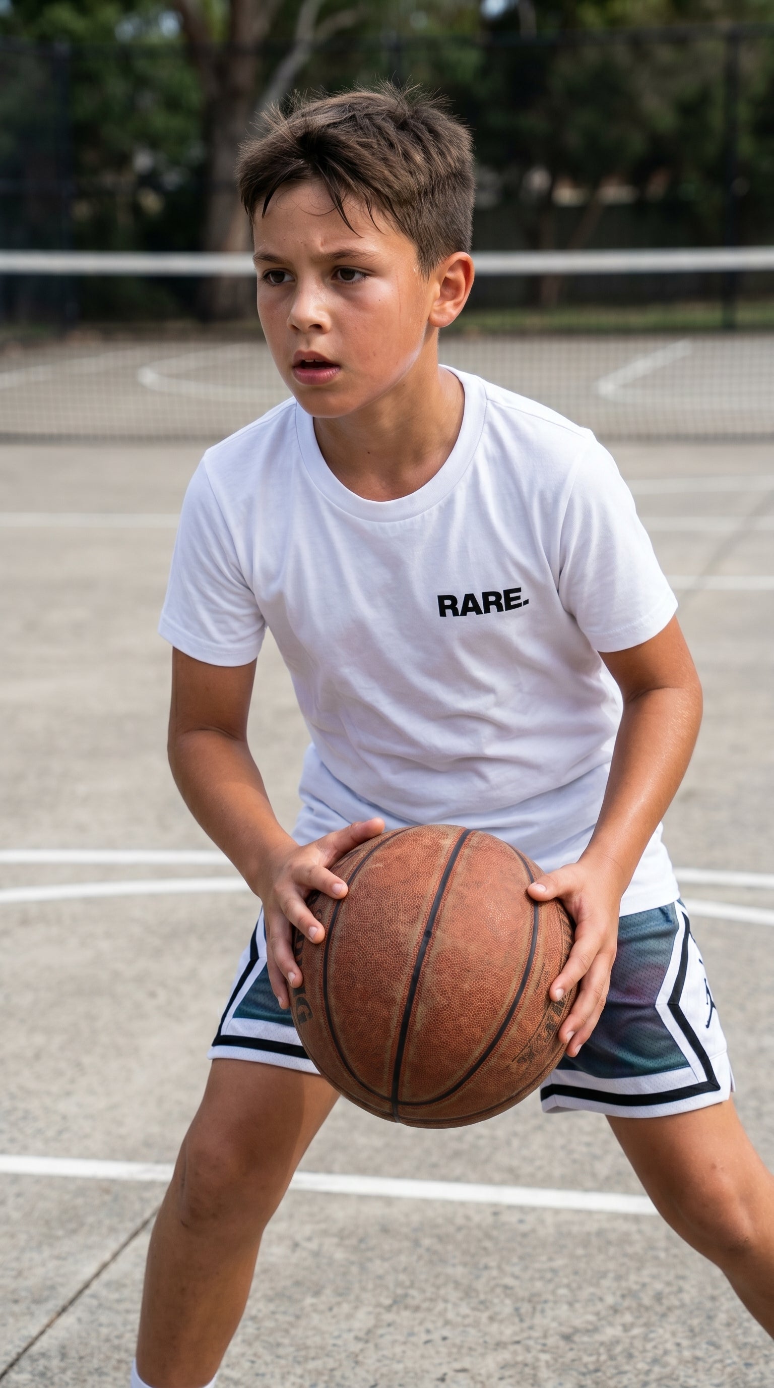 Child holding a basketball on a court wearing a white t-shirt with 'RARE' printed on it.