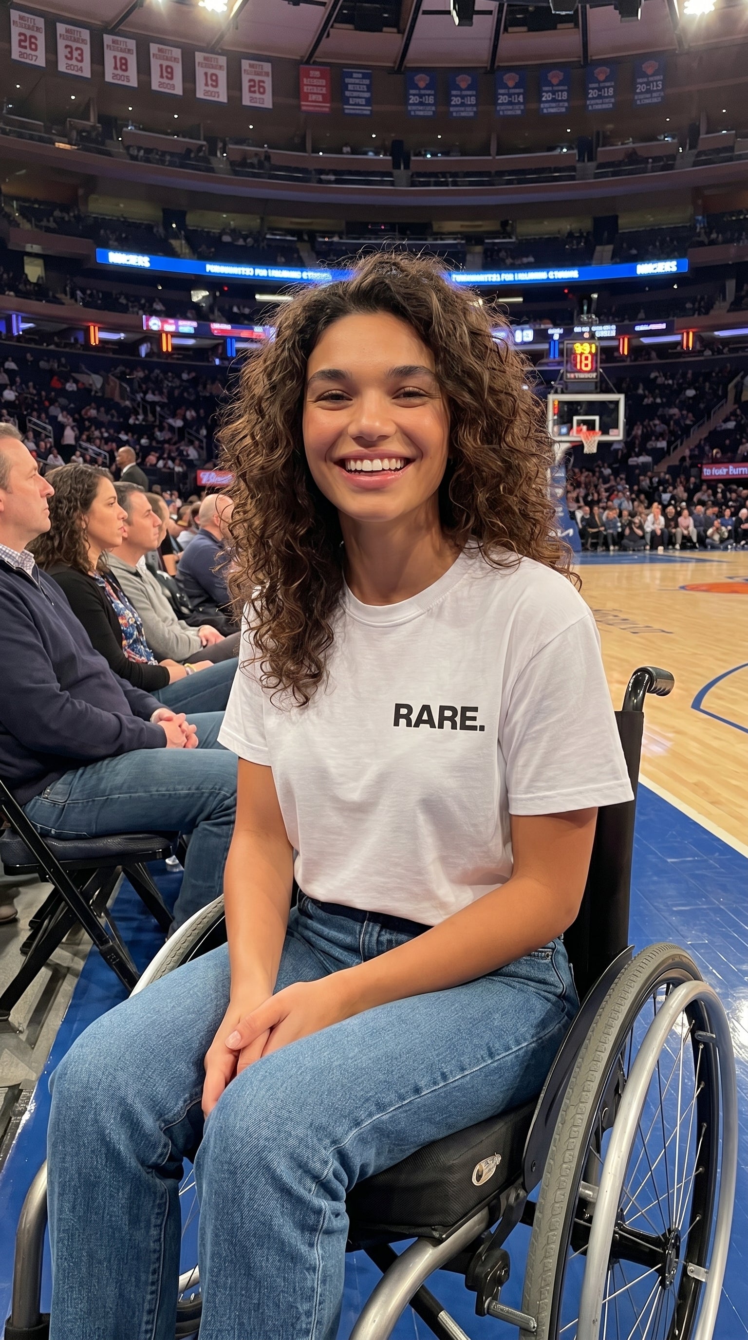 Person in a wheelchair wearing a 'RARE.' shirt at a sports event.