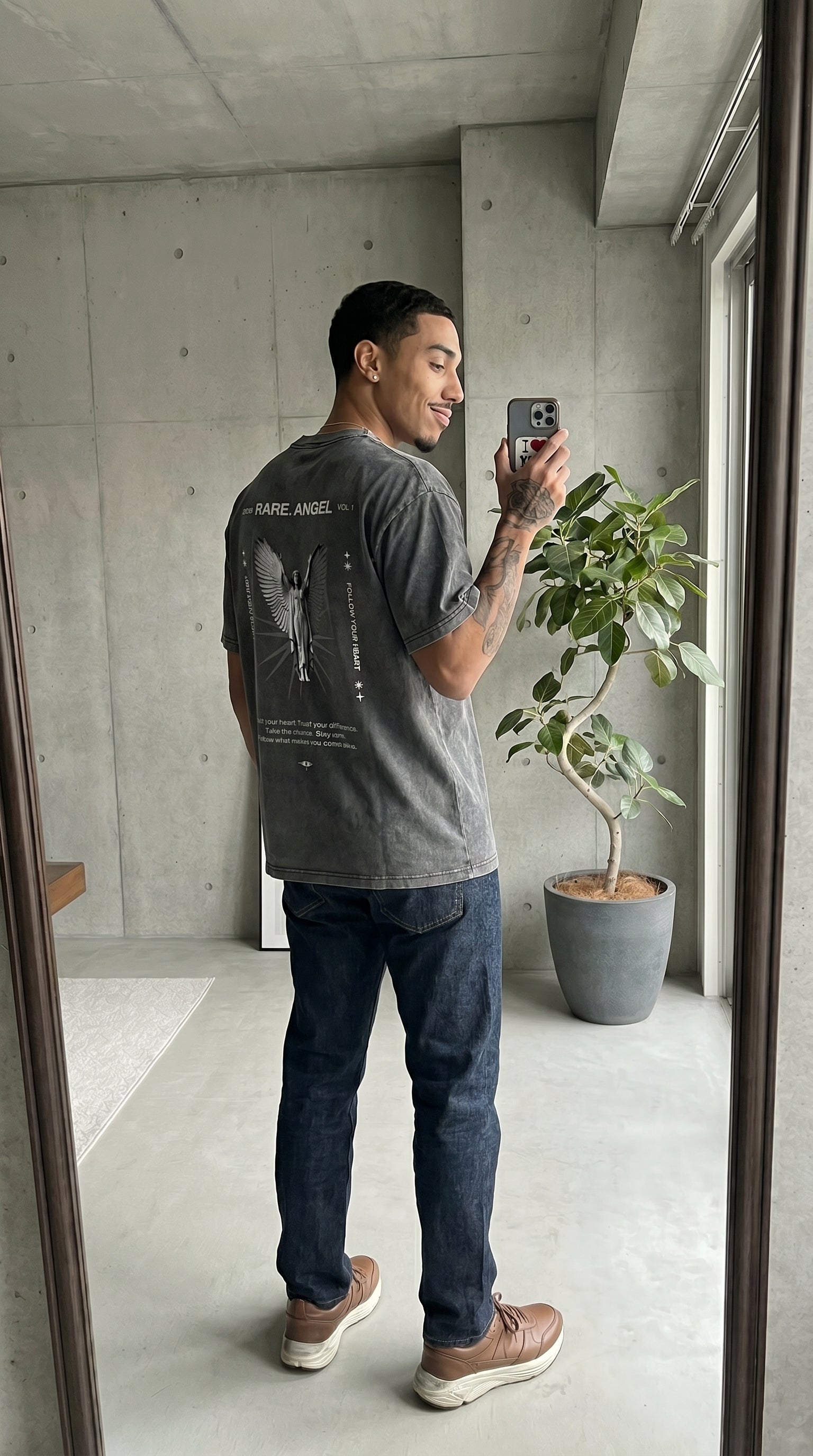 Man taking a mirror selfie wearing a gray t-shirt with text and graphics.