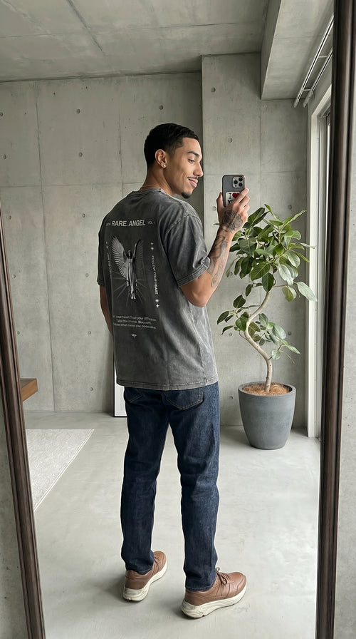 Man taking a mirror selfie wearing a gray t-shirt with text and graphics.